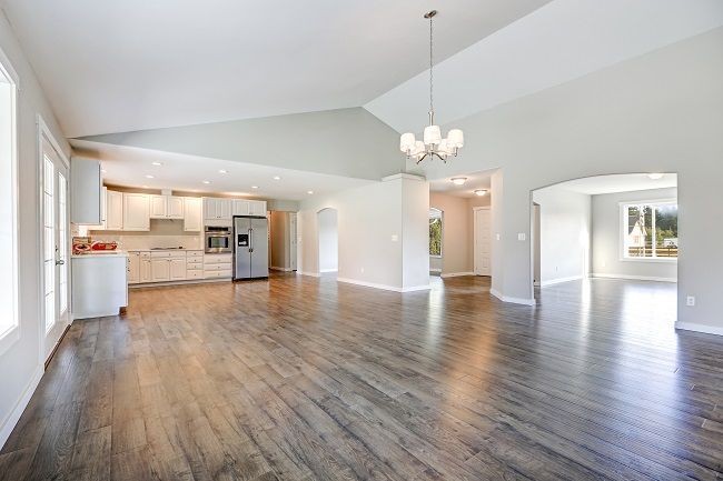 Spacious empty living area with hardwood floors, modern kitchen, and a hanging light fixture.