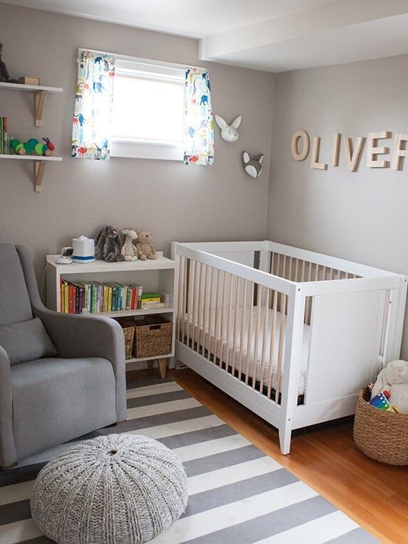 Cozy nursery with a white crib, bookshelf, gray chair, and striped rug.